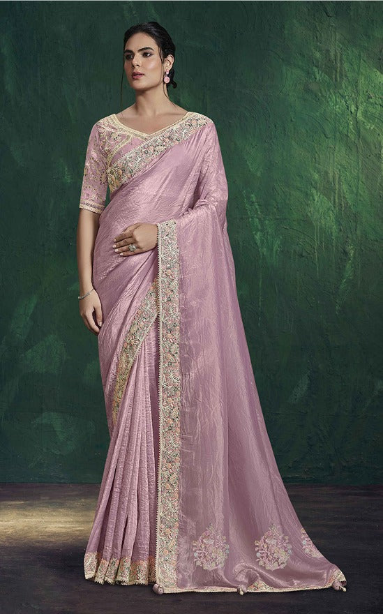 Woman wearing a pink saree with gold embroidery against a dark green background