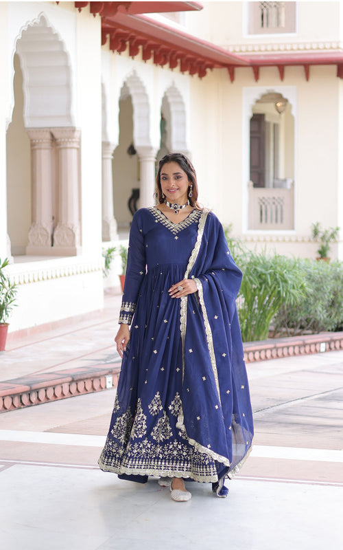 Woman in a blue traditional outfit standing in front of an architectural building.