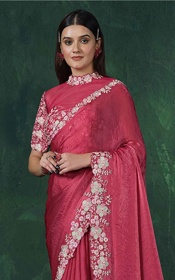 Woman wearing a pink saree with floral patterns against a green background