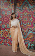 Woman in a beige saree standing against a colorful geometric-patterned wall.