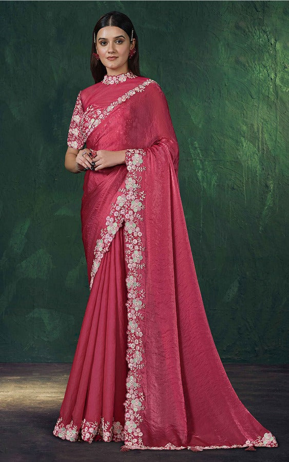 Woman wearing a pink saree with white floral embroidery against a dark green background