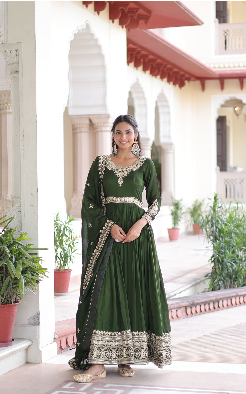 Woman in a green traditional outfit standing in front of an architectural building with plants.