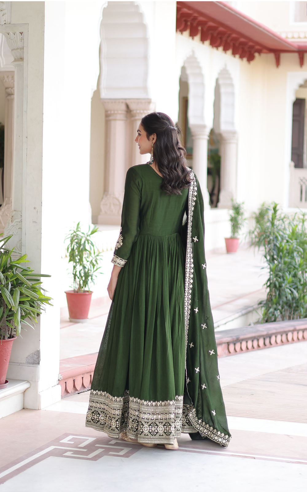 Woman in a green traditional outfit standing in front of an architectural building with plants.