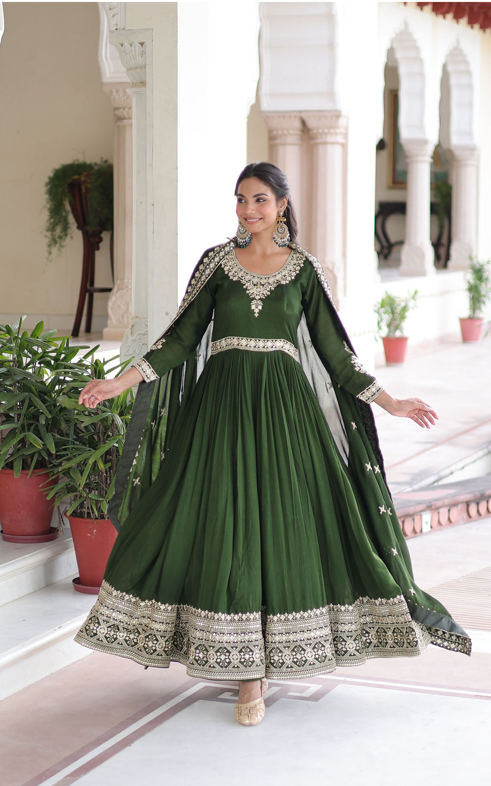 Woman in a green traditional outfit with white embroidery standing in an elegant indoor setting.