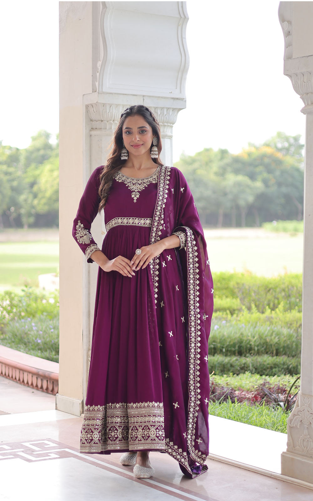 Woman in a purple traditional outfit standing on a porch with greenery in the background