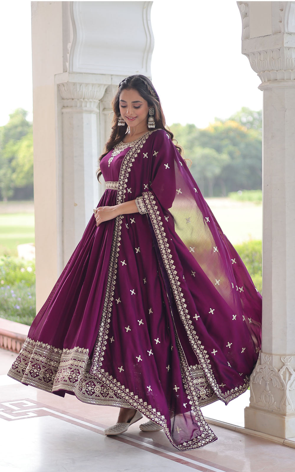 Woman in a purple traditional outfit with gold embroidery standing in a decorative doorway.