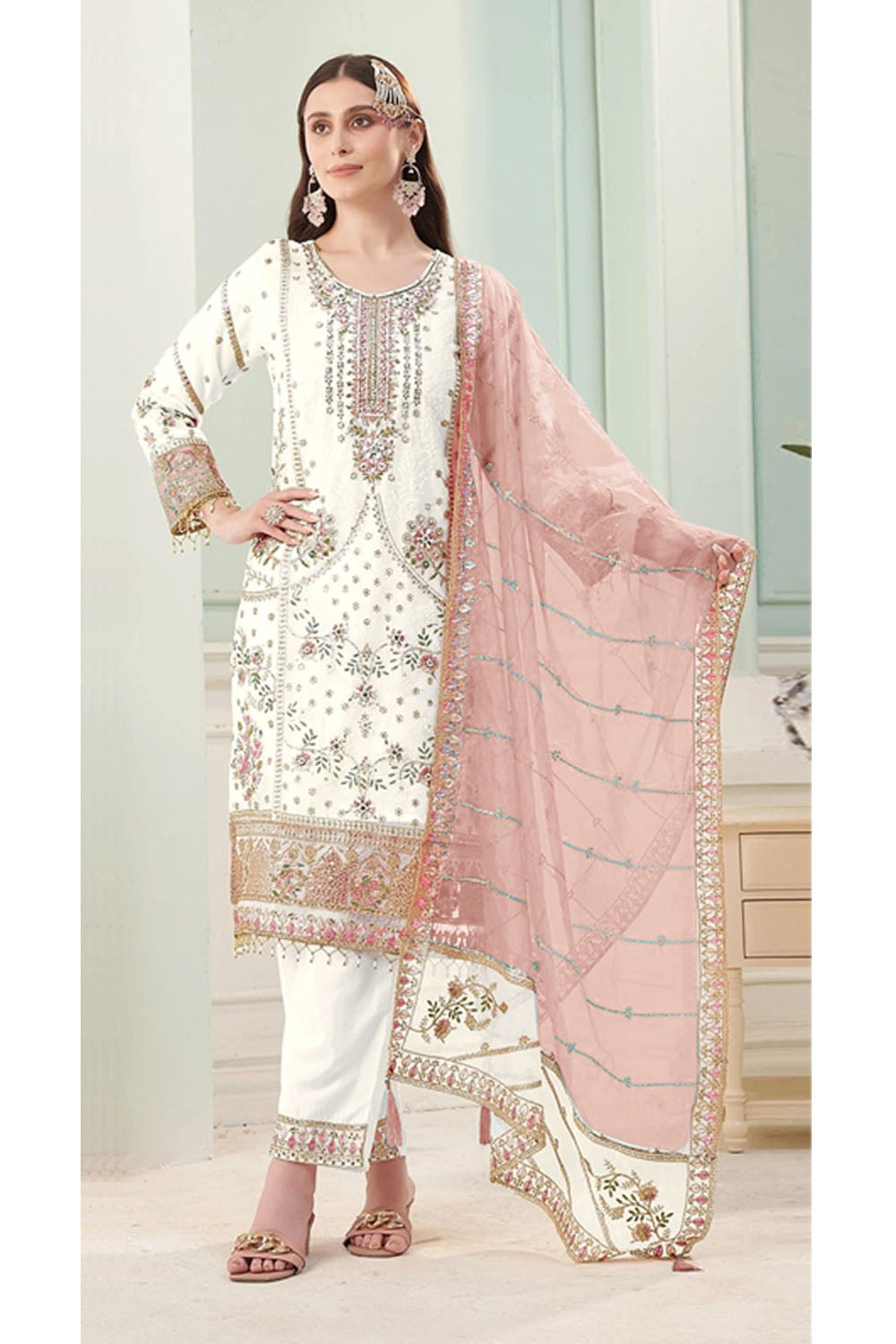 Woman wearing a traditional outfit with white and pink embroidery in a light interior setting
