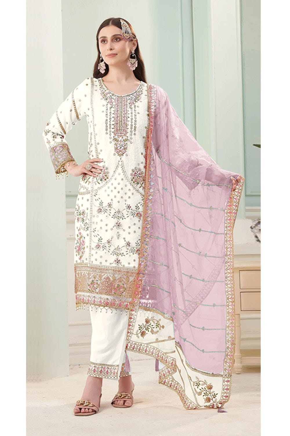 Woman wearing a traditional outfit with a white and pink embroidered dupatta in a light-colored room.
