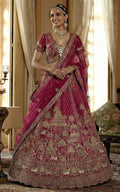 Woman in a traditional pink and gold embroidered saree with jewelry in an elegant indoor setting.