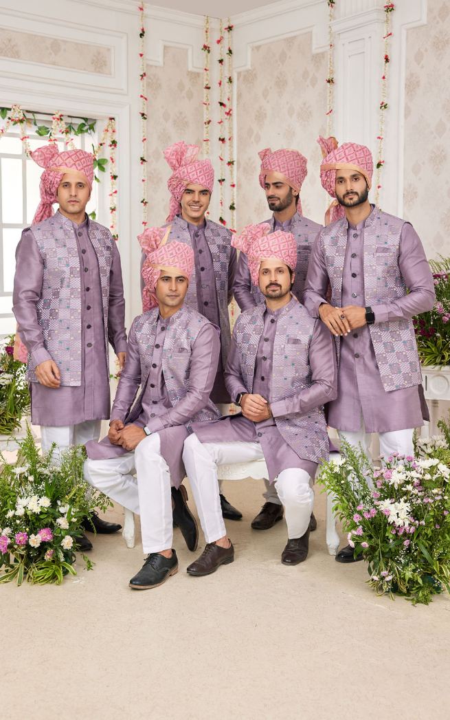 Men in traditional lavender sherwanis with pink turbans posing in a decorated indoor setting.