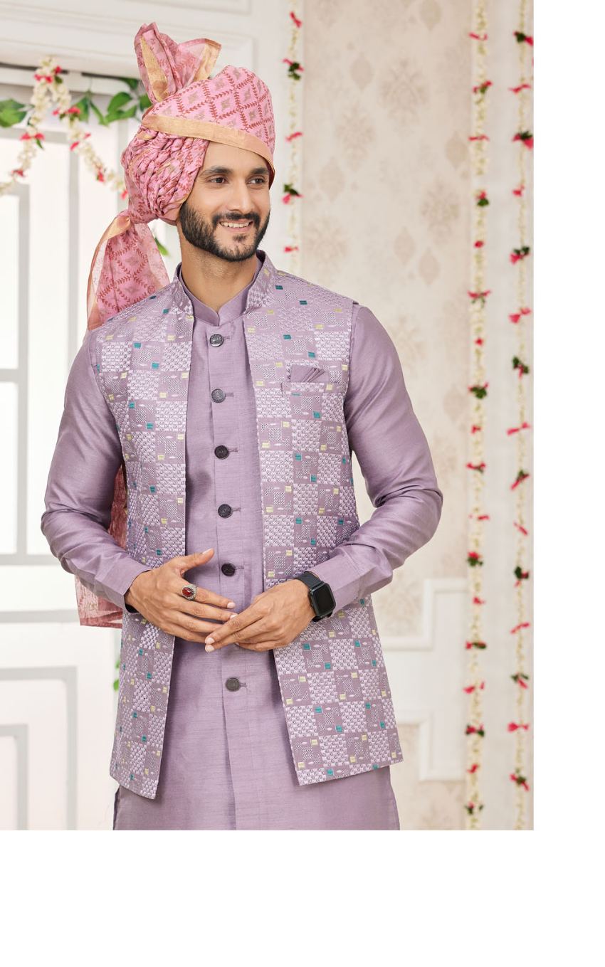 Man wearing a traditional jacket with a pink turban and matching vest in a decorated indoor setting.