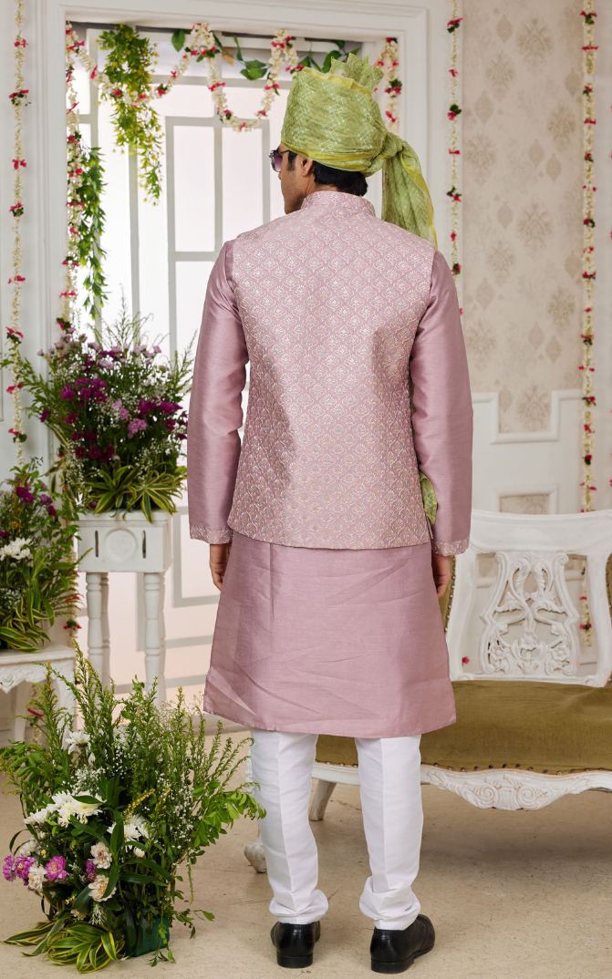 Person wearing a traditional pink sherwani with white pants in a decorated room.