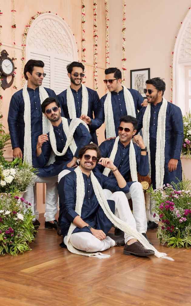 Group of men in formal attire with white scarves in a decorated indoor setting