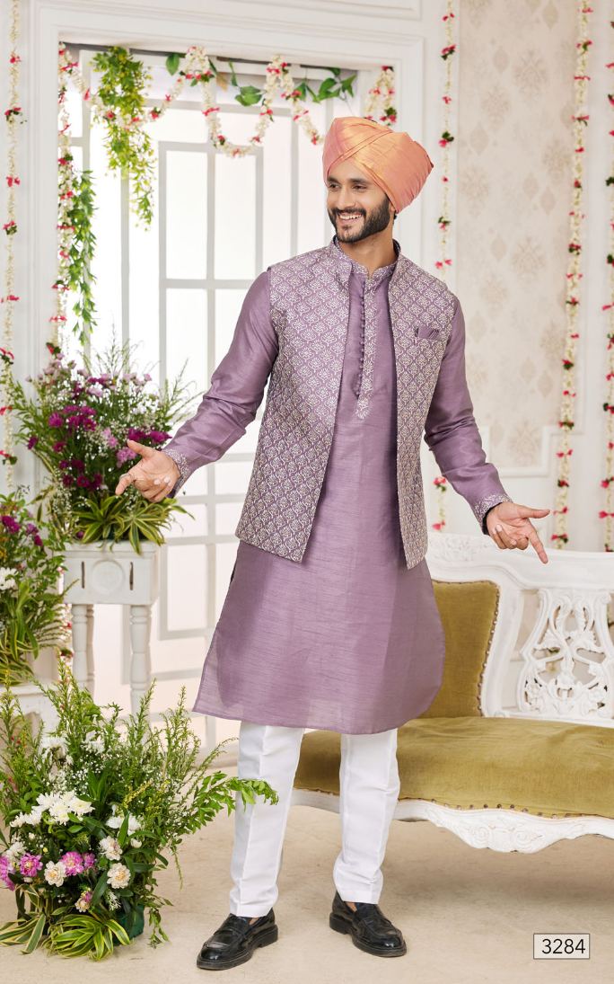 Man in traditional lavender kurta with white pants holding flowers indoors.
