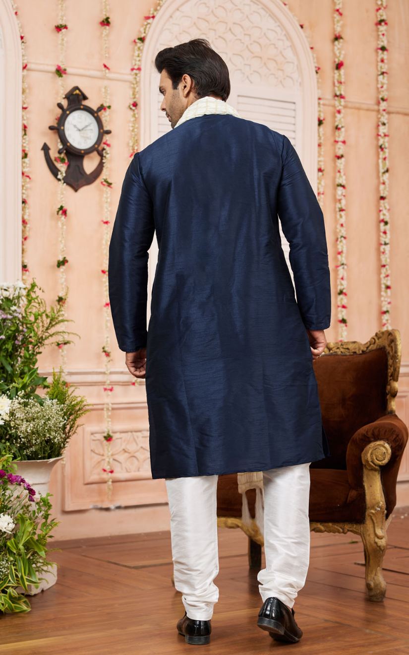Man wearing a navy blue sherwani with white pants in an indoor setting.