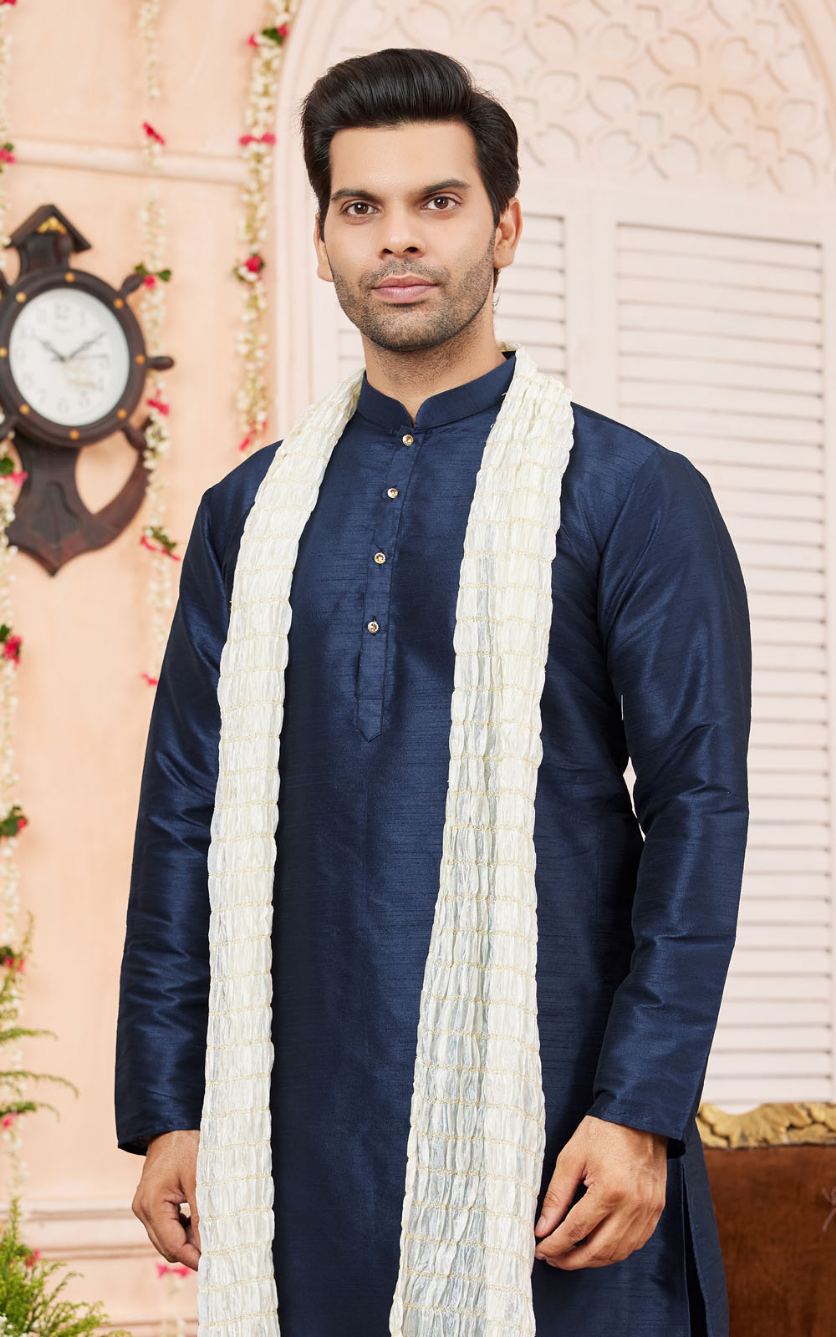 Man wearing a navy kurta with a white scarf against a decorative wall.