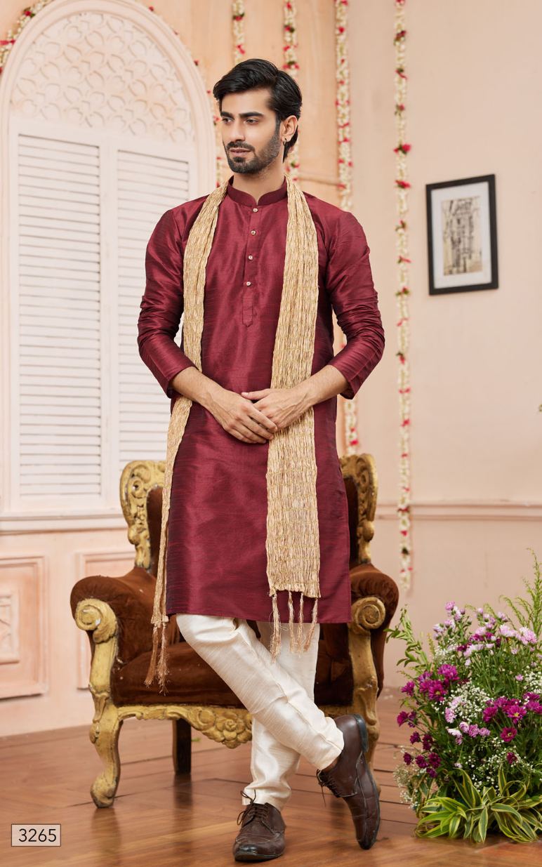 Man wearing a maroon kurta with white pants and a beige scarf, standing in a decorated room.