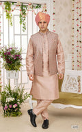 Man wearing a traditional pink kurta with a matching jacket and turban, standing in a decorated room with flowers.