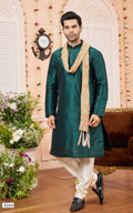 Man wearing a green kurta with white pants and a beige scarf in a decorated room.