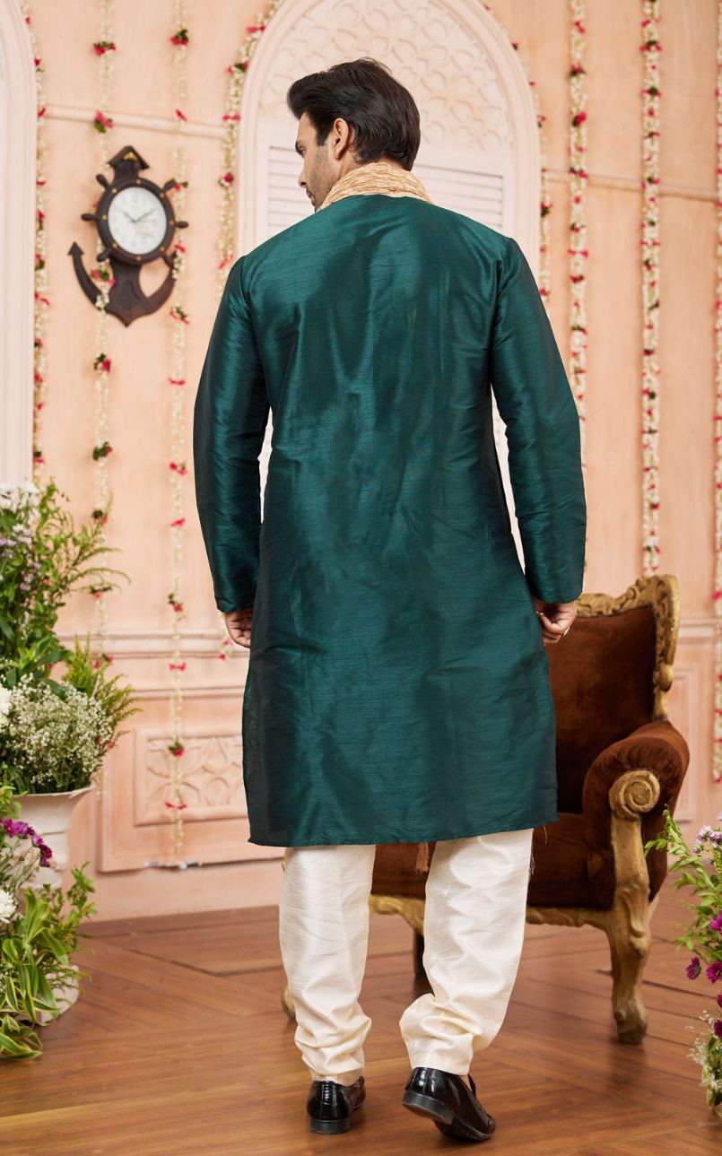Man wearing a green sherwani with white pants in a decorated room.