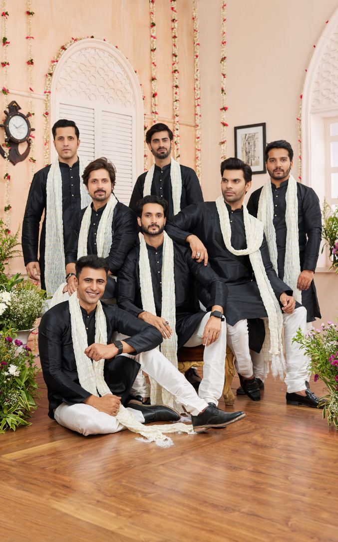 Group of men in formal attire with white scarves in a decorated indoor setting.