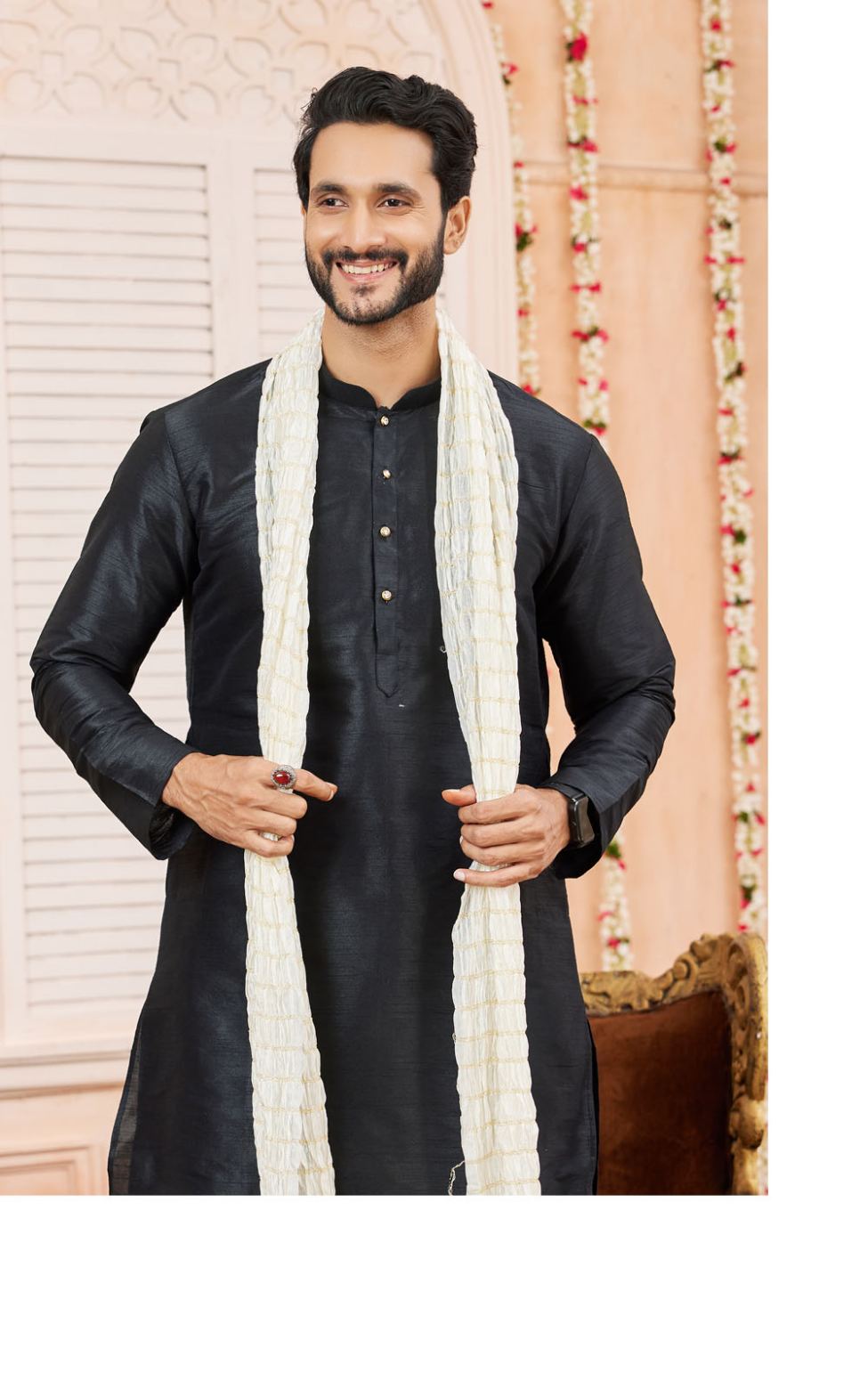 Man wearing a black kurta with a white scarf against a decorative background