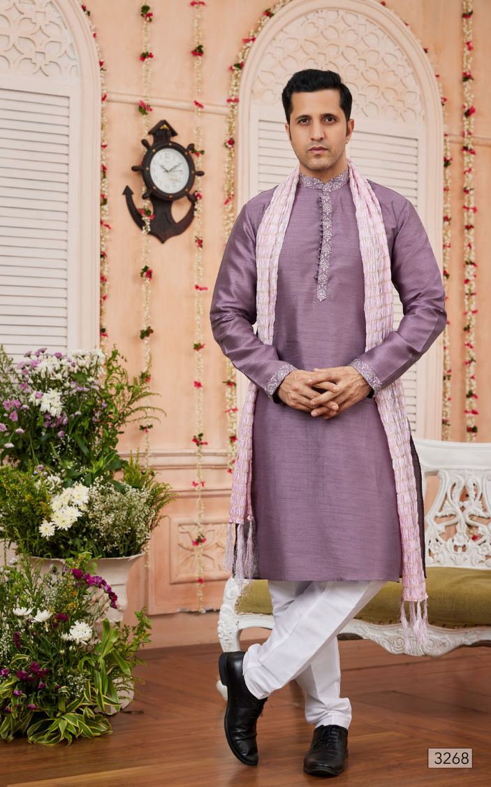 Man wearing a purple kurta with white pants in a decorated room with flowers and a clock.