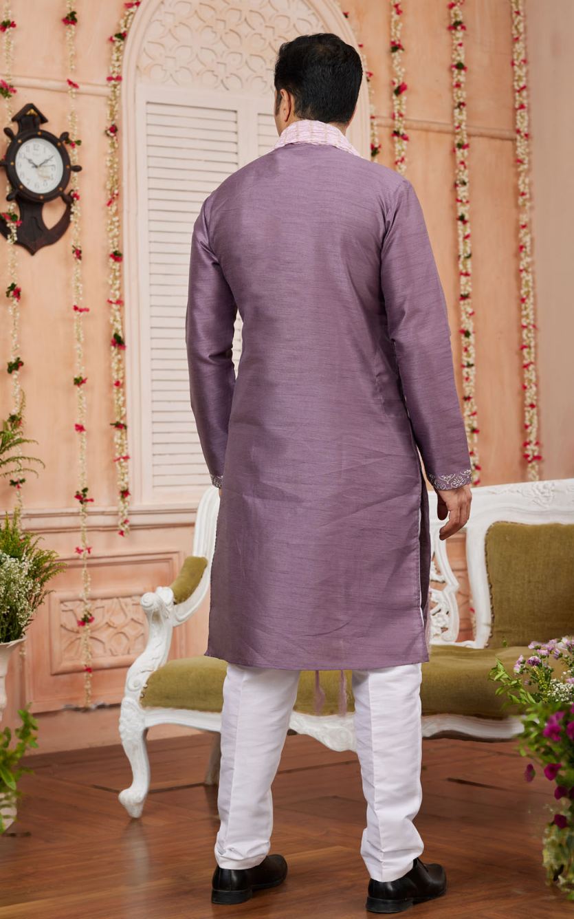 Man wearing a purple kurta with white pants in a decorated room.