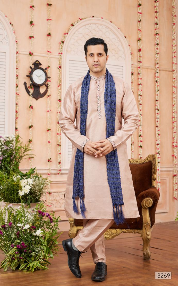 Man wearing a traditional kurta with a blue shawl in a decorated room.
