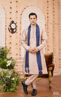 Man wearing a traditional kurta with a blue shawl in a decorated room.
