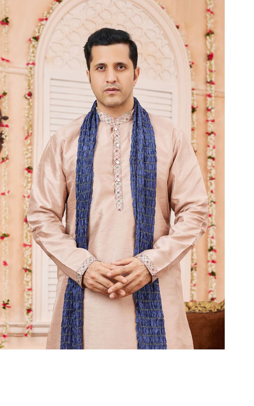 Man wearing a traditional outfit with a blue scarf against a decorative background