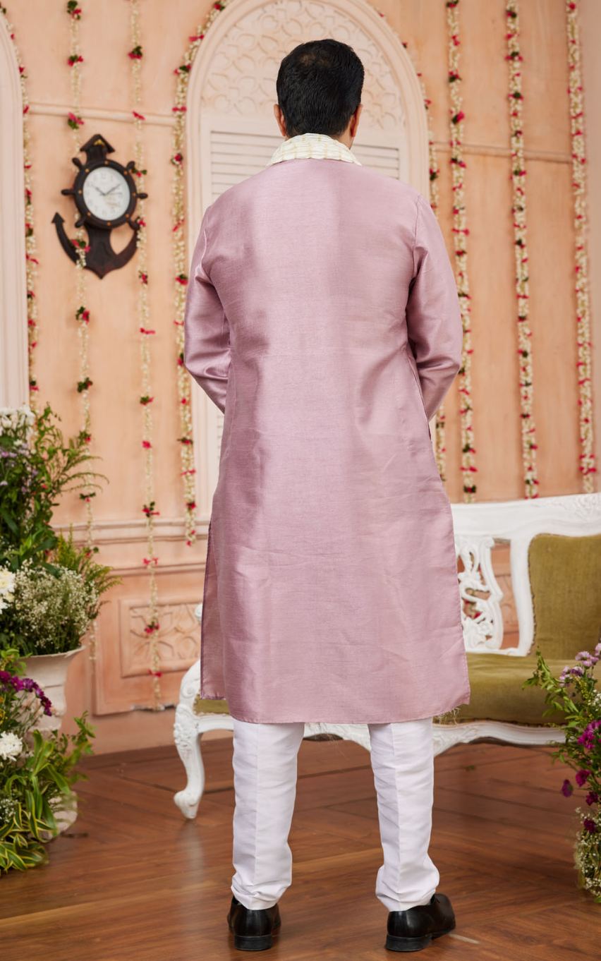 Man wearing a pink sherwani in a decorated room with flowers and a clock.