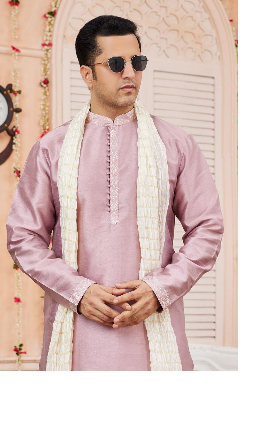 Man wearing a pink kurta with a white shawl in a decorated room.