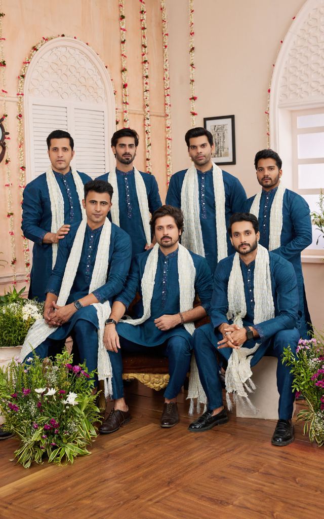 Group of men in formal blue attire with white scarves in a decorated indoor setting.