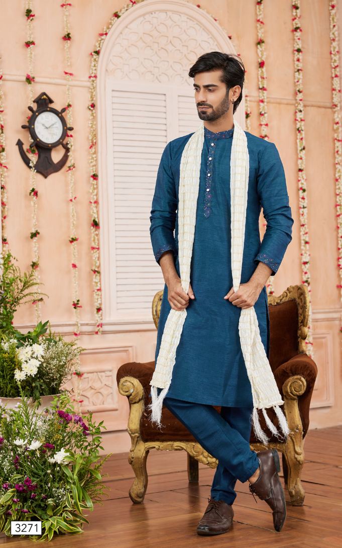 Man wearing a blue kurta with a white scarf in a decorated room.